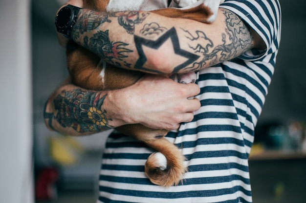 Kostenloses Foto junger trendiger hipster mit tätowierungen verrücktes lockiges haar kuschelt seinen kleinen besten freund