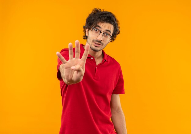 Junger überraschter Mann im roten Hemd mit optischer Brille gestikuliert vier Handzeichen lokalisiert auf orange Wand
