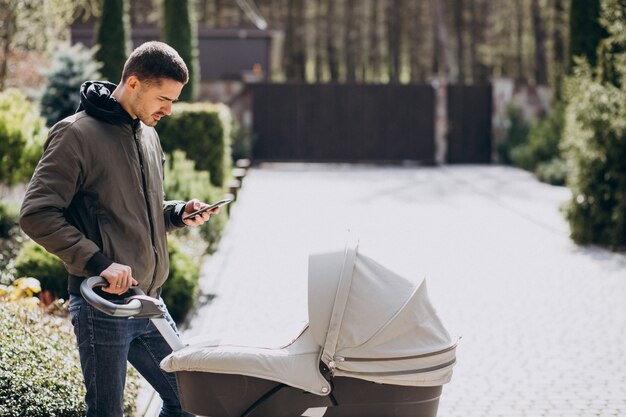 Junger Vater, der mit Kinderwagen im Park geht