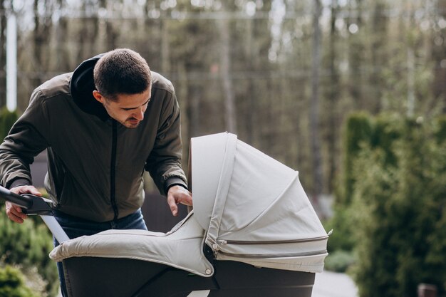 Junger Vater, der mit Kinderwagen im Park geht