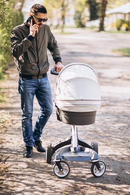 Junger Vater, der mit Kinderwagen im Park geht