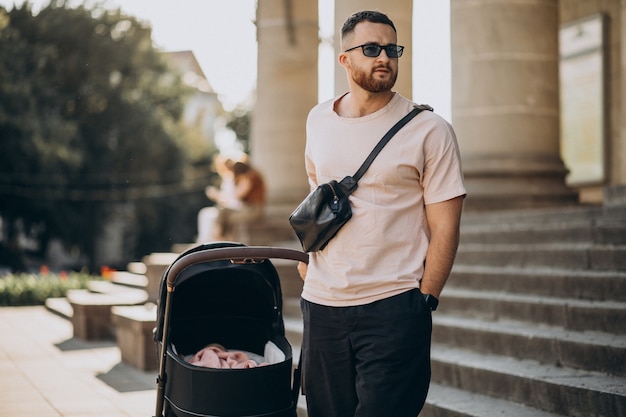 Junger Vater, der mit seinem Baby in einem Kinderwagen hinausgeht