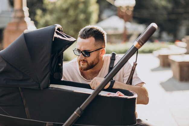 Junger Vater, der mit seinem Baby in einem Kinderwagen hinausgeht