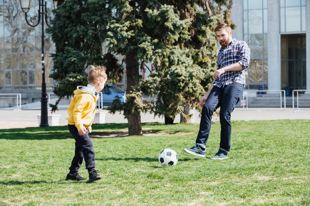 Junger Vater und sein Sohn spielen Fußball in einem Park