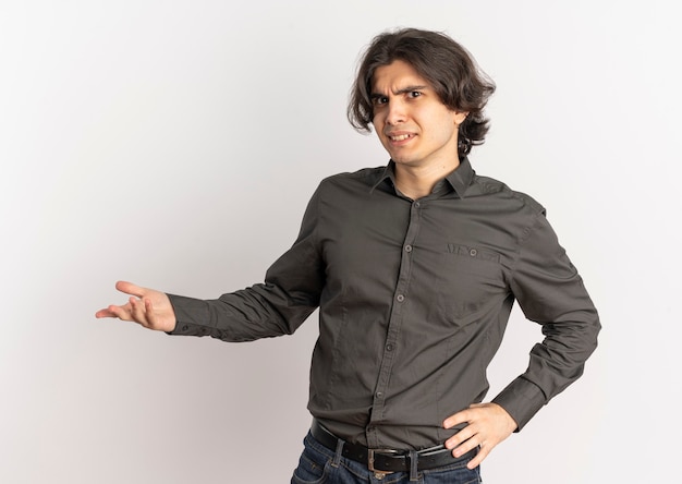 Junger verärgerter hübscher kaukasischer Mann hält Hand offen und betrachtet Kamera lokalisiert auf weißem Hintergrund mit Kopienraum