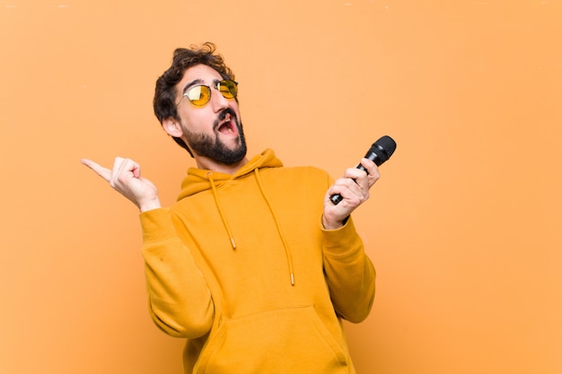 Junger verrückter cooler mann mit einem mikrofon auf orange wand