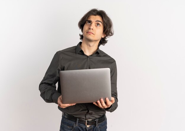 Junger verwirrter hübscher kaukasischer Mann hält Laptop und schaut lokalisiert auf weißem Hintergrund mit Kopienraum auf