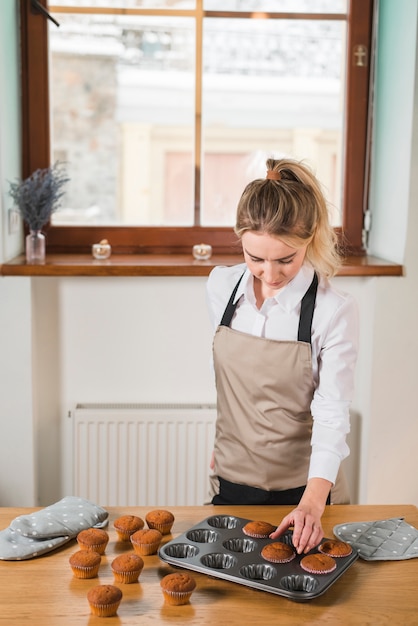 Junger weiblicher bäcker, der die muffins vom kuchenformbehälter entfernt