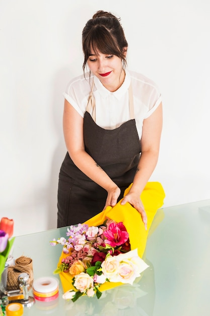 Junger weiblicher Florist, der Blumen im gelben Stoff auf Schreibtisch einwickelt