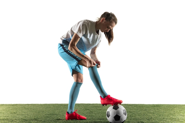 Junger weiblicher Fußball- oder Fußballspieler mit langen Haaren in Sportbekleidung und Stiefeln, die sich auf das Spiel vorbereiten, lokalisiert auf weißem Hintergrund. Konzept des gesunden Lebensstils, des Profisports, des Hobbys.