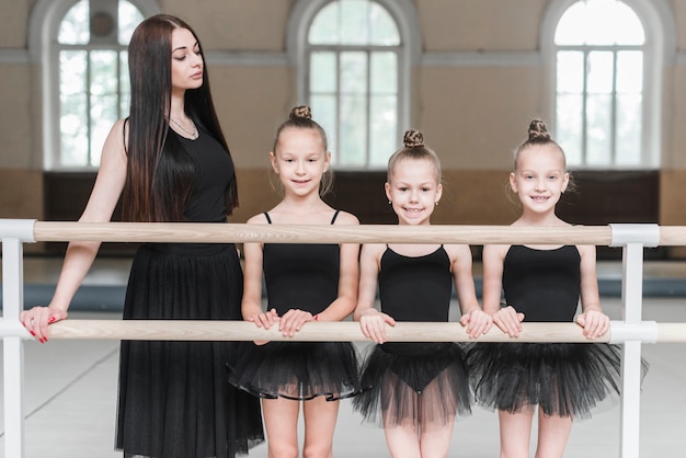 Junger weiblicher Trainer mit ihren drei Ballerinamädchen, die hinter dem Barre stehen