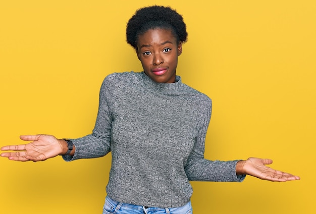 Junges afroamerikanisches Mädchen in lässiger Kleidung, ahnungsloser und verwirrter Gesichtsausdruck mit Armen und Händen, der Zweifel an dem Konzept aufkommen lässt
