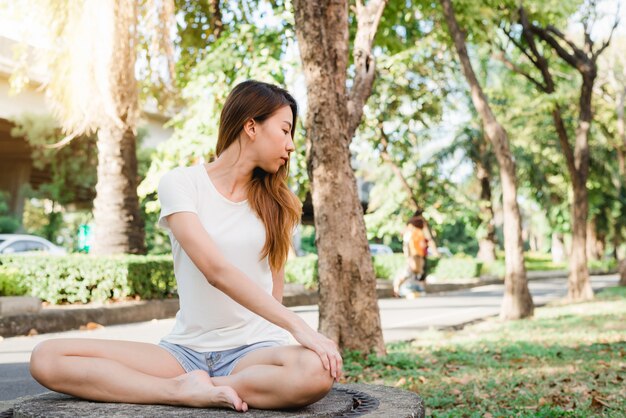 Junges asiatisches Frauenyoga draußen halten ruhig und meditieren beim Üben von Yoga