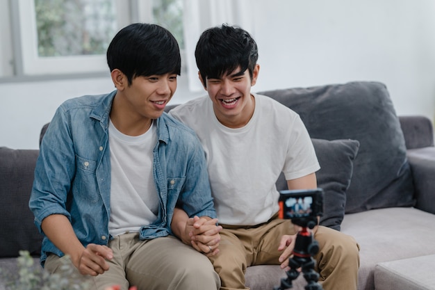 Junges asiatisches homosexuelles Paarinfluencer-Paar vlog zu Hause. Die jugendlich koreanischen glücklichen LGBTQ-Männer entspannen sich Spaß unter Verwendung des Kameraaufzeichnungs-vlog-Video-Uploads in Social Media beim Lügensofa im Wohnzimmer am Haus.