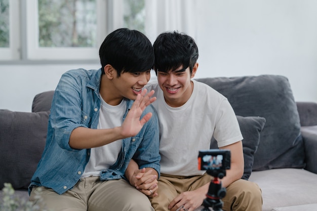 Junges asiatisches homosexuelles Paarinfluencer-Paar vlog zu Hause. Die jugendlich koreanischen glücklichen LGBTQ-Männer entspannen sich Spaß unter Verwendung des Kameraaufzeichnungs-vlog-Video-Uploads in Social Media beim Lügensofa im Wohnzimmer am Haus.