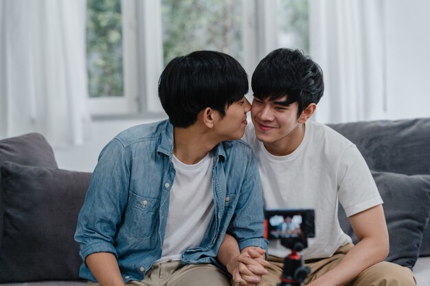 Junges asiatisches homosexuelles Paarinfluencer-Paar vlog zu Hause. Die jugendlich koreanischen glücklichen LGBTQ-Männer entspannen sich Spaß unter Verwendung des Kameraaufzeichnungs-vlog-Video-Uploads in Social Media beim Lügensofa im Wohnzimmer am Haus.