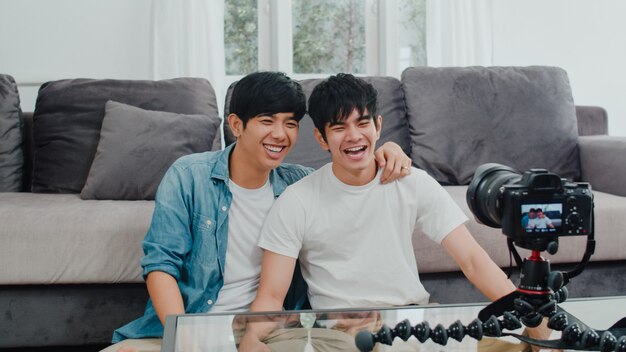 Junges asiatisches homosexuelles Paarinfluencer-Paar vlog zu Hause. Die jugendlich koreanischen glücklichen LGBTQ-Männer entspannen sich Spaß unter Verwendung des Kameraaufzeichnungs-vlog-Video-Uploads in Social Media beim Lügensofa im Wohnzimmer am Haus.