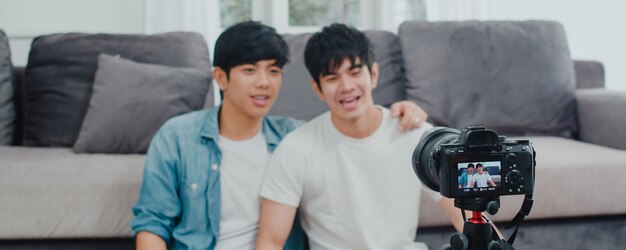 Junges asiatisches homosexuelles Paarinfluencer-Paar vlog zu Hause. Die jugendlich koreanischen glücklichen LGBTQ-Männer entspannen sich Spaß unter Verwendung des Kameraaufzeichnungs-vlog-Video-Uploads in Social Media beim Lügensofa im Wohnzimmer am Haus.