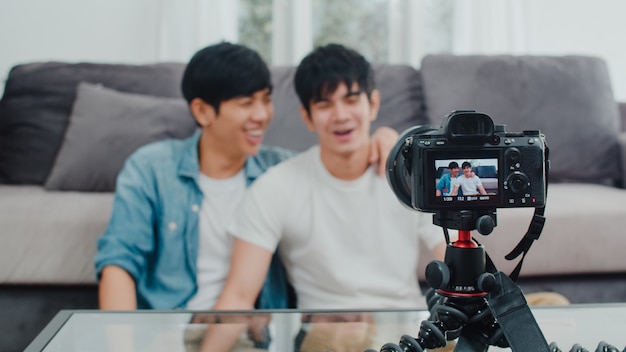 Junges asiatisches homosexuelles paarinfluencer-paar vlog zu hause. die jugendlich koreanischen glücklichen lgbtq-männer entspannen sich spaß unter verwendung des kameraaufzeichnungs-vlog-video-uploads in social media beim lügensofa im wohnzimmer am haus.