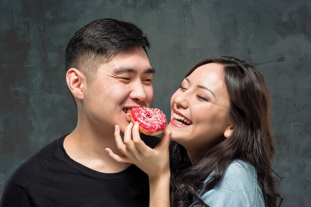 Junges asiatisches Paar genießt das Essen des süßen bunten Donuts