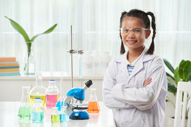 Junges asiatisches Schulmädchen, das im Chemieunterricht mit bunten Phiolen aufwirft
