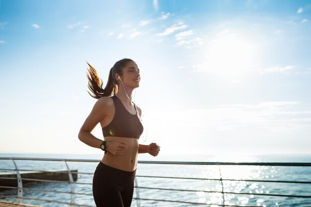 junges attraktives Fitnessmädchen, das mit Meer auf Hintergrund joggt