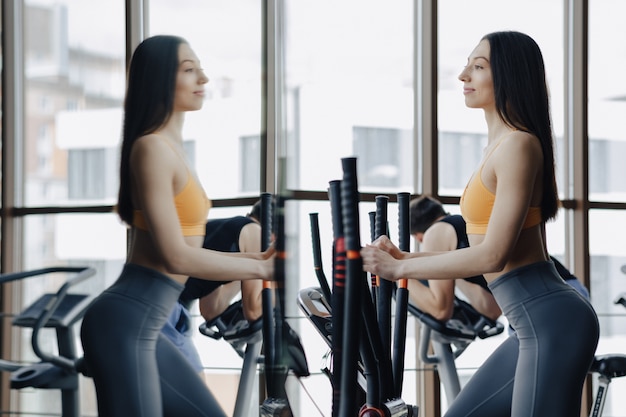 Junges attraktives Mädchen an der Turnhalle auf Hometrainer, Eignung und Yoga