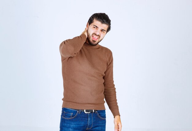 Junges attraktives Modell im braunen Pullover, der Gesten über der weißen Wand macht.