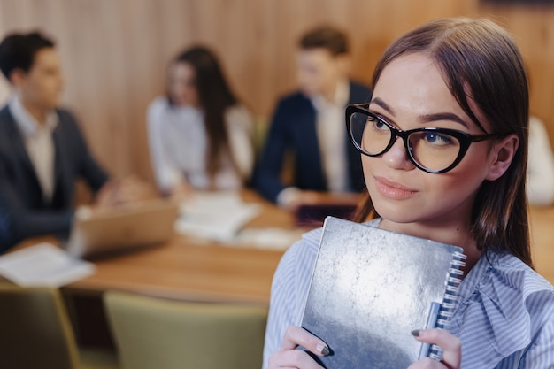 Junges attraktives stilvolles Büroangestelltmädchen in den Gläsern mit einem Notizbuch in den Händen