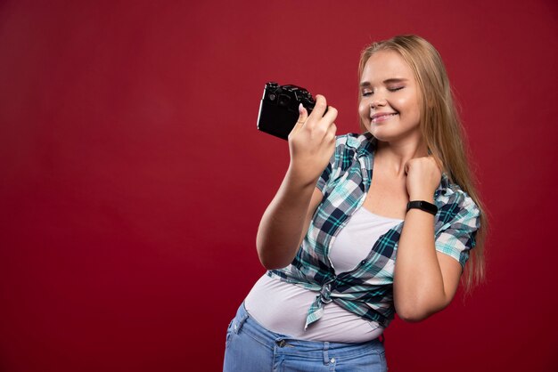 Junges blondes Foto hält eine professionelle Kamera und nimmt ihr Selfie in schönen und selbstbewussten Positionen auf.