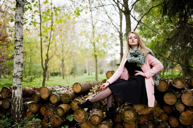 Junges blondes Mädchen im rosafarbenen Mantel posierte vor Holzstümpfen im Hintergrund