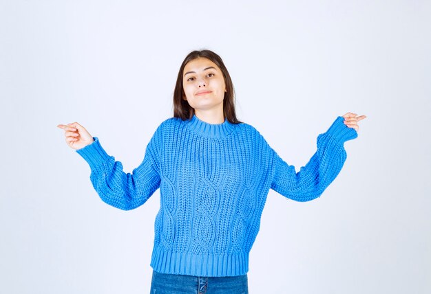 Junges Brunettemädchen in der blauen Strickjacke, die auf Weiß aufwirft.