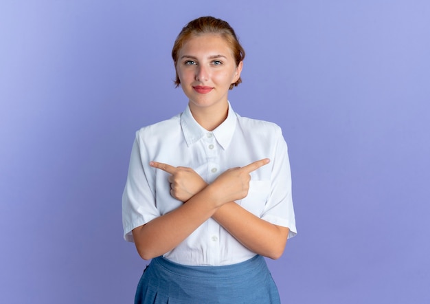 Kostenloses Foto junges erfreutes blondes russisches mädchen zeigt auf seiten lokalisiert auf lila hintergrund mit kopienraum