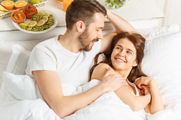 Junges erwachsenes heterosexuelles paar, das auf bett im schlafzimmer liegt
