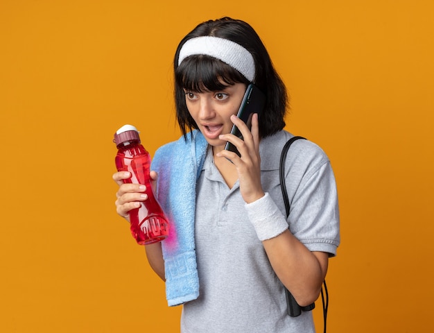 Kostenloses Foto junges fitness-mädchen mit stirnband mit handtuch auf der schulter mit wasserflasche