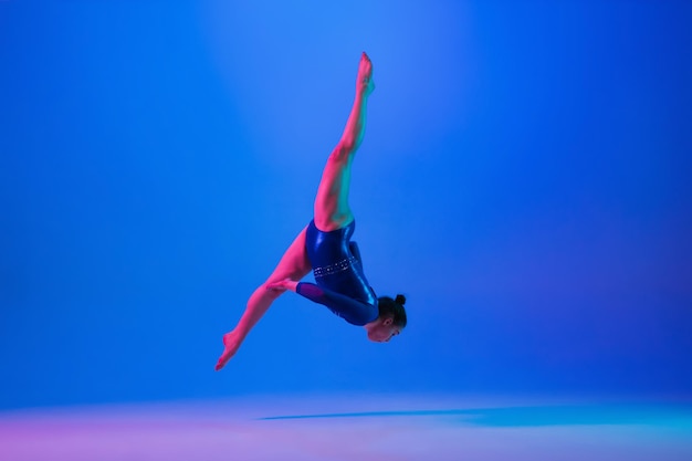 Junges flexibles Mädchen, das auf blauem Studiohintergrund isoliert ist Junges weibliches Modell, das künstlerische Gymnastik praktiziert Übungen für Flexibilitätsbalance