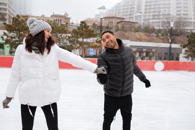 Junges glückliches liebendes Paar, das an Eisbahn im Freien skatet