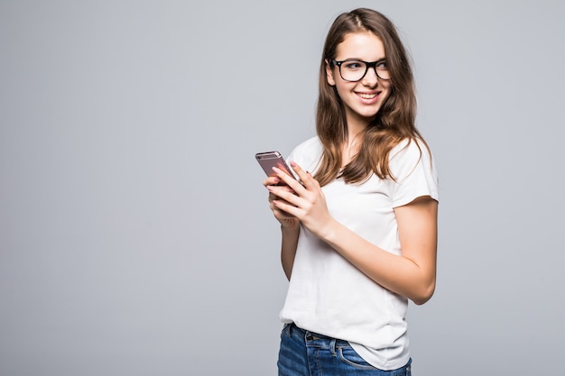 Junges glückliches Mädchen in den Gläsern im weißen T-Shirt und in den blauen Jeans vor dem weißen Studiohintergrund