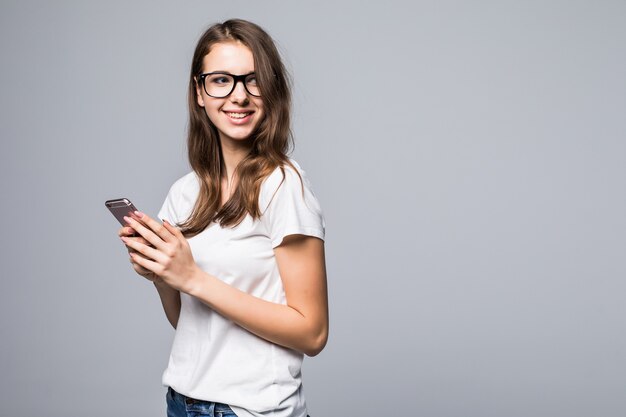 Junges glückliches Mädchen in den Gläsern im weißen T-Shirt und in den blauen Jeans vor dem weißen Studiohintergrund