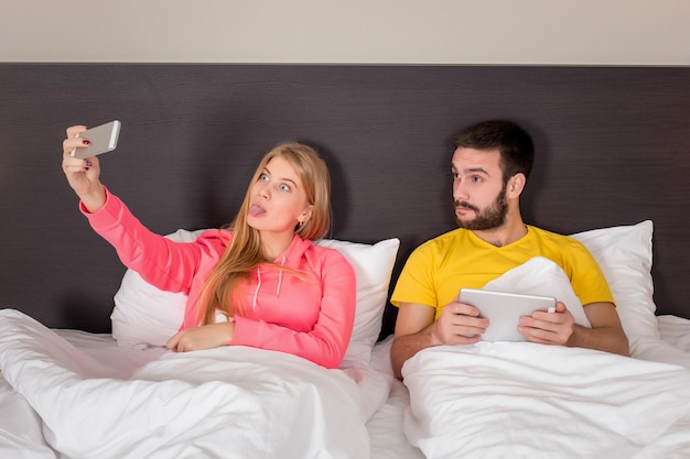 Junges glückliches Paar auf dem Bett, das Selfie mit Telefonkamera macht. Konzept über Technologie und Menschen
