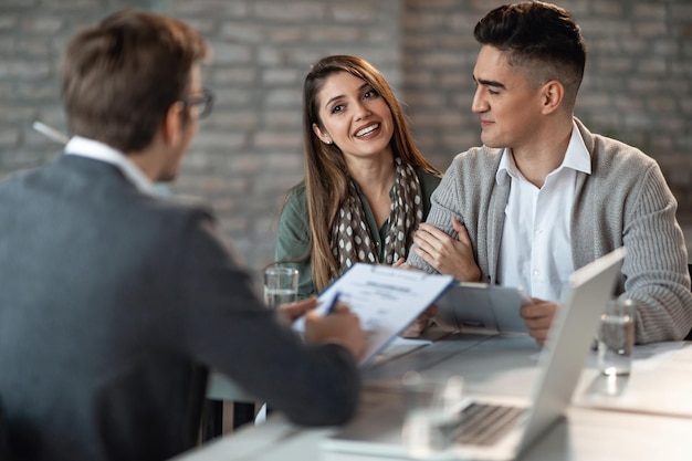 Junges glückliches Paar, das ein Treffen mit einem Immobilienmakler im Büro hat Der Fokus liegt auf der Frau