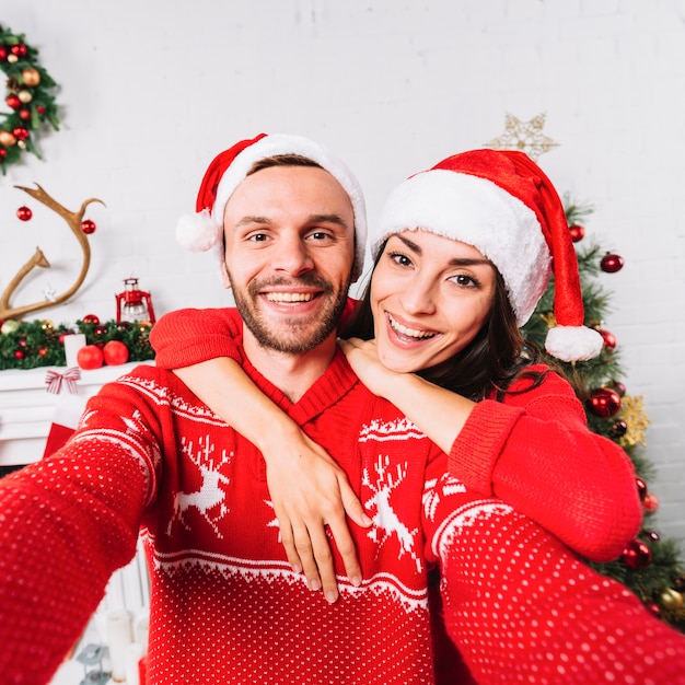 Junges glückliches Paar, das in den Weihnachtshüten umfasst