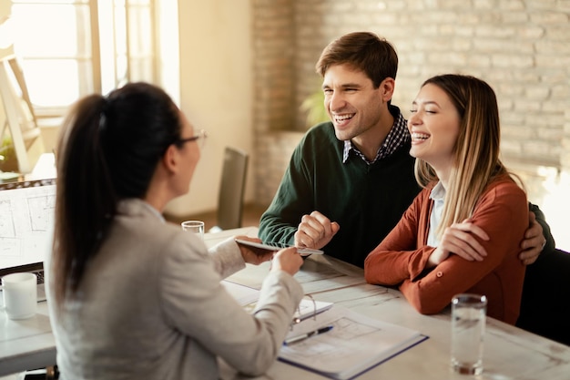 Junges glückliches Paar, das mit einem Finanzberater kommuniziert, der während eines Meetings ein digitales Tablet verwendet