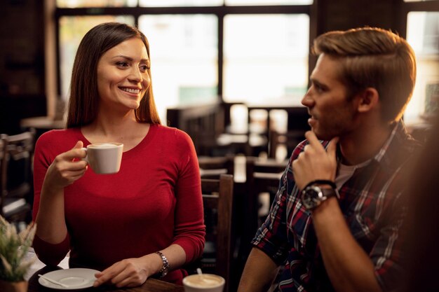 Junges glückliches Paar, das miteinander spricht, während es in einem Café Kaffee trinkt. Der Fokus liegt auf der Frau