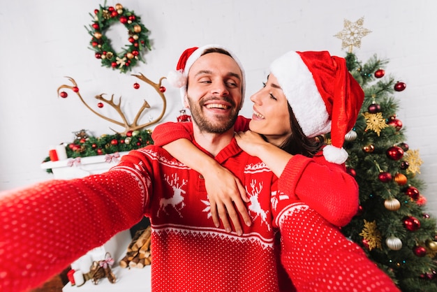 Junges glückliches Paar, das nahe Weihnachtsbaum umfasst