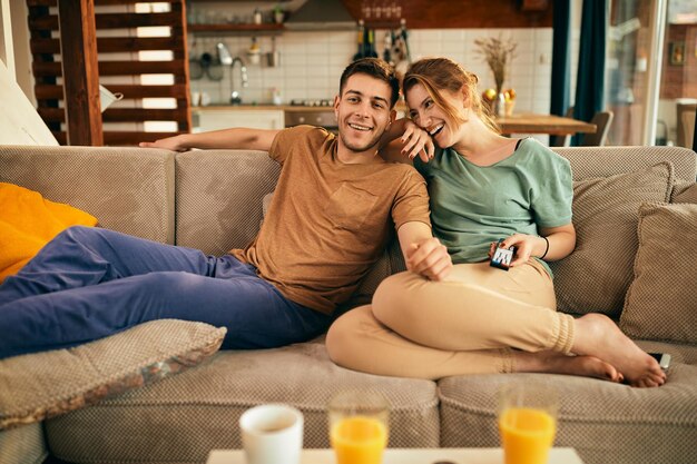 Junges glückliches Paar, das sich auf dem Sofa entspannt und zu Hause fernsieht