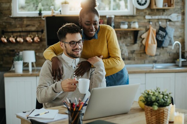 Junges glückliches Paar, das zu Hause eine E-Mail auf dem Laptop liest