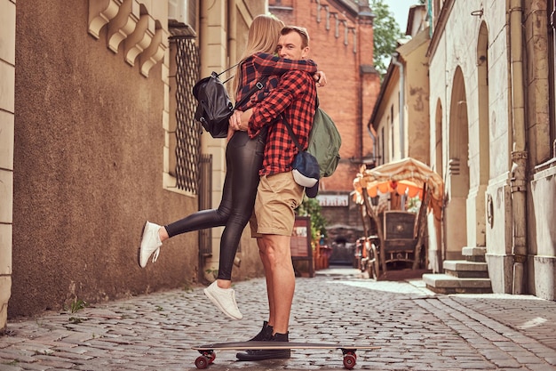 Junges Hipster-Paar, hübscher Skater und seine Freundin kuscheln, während sie auf alten engen Straßen Europas stehen.