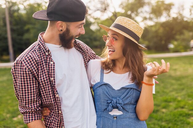 Junges hübsches Hipster-Paar, das im Park spazieren geht und lacht, Freunde, die Spaß zusammen haben, Romantik am Datum, Sommermode-Stil, buntes Hipster-Outfit, Mann und Frau lächelnd umarmen