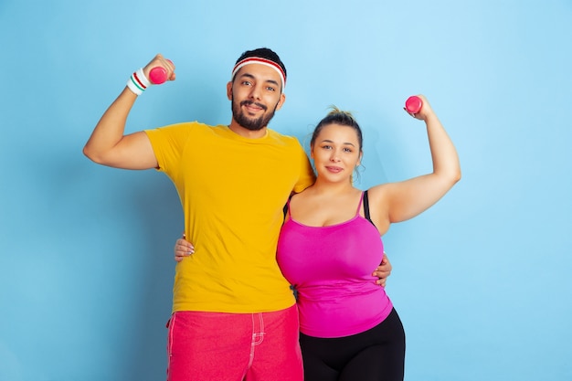 Junges hübsches kaukasisches Paar im hellen Kleidertraining auf blauem Raum Konzept des Sports, der menschlichen Gefühle, des Ausdrucks, des gesunden Lebensstils, der Beziehung, der Familie